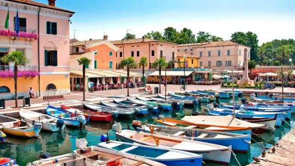 Barche ormeggiate nel **bardolino hafen**, con edifici colorati e palme sullo sfondo.