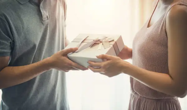 Mężczyzna wręcza kobiecie prezent z okazji 25 rocznicy ślubu. Delikatne wstążki zdobią pudełko.