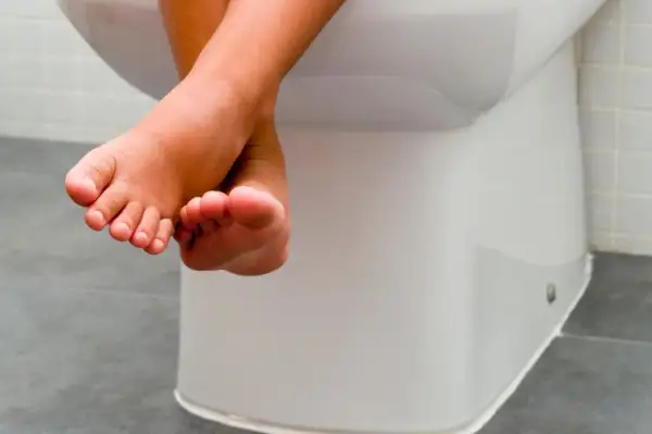 Kleine Füße baumeln über der Toilette. Tipps, wie Kinder trocken werden, sind hier wichtig.