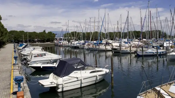 Barche a vela e a motore ormeggiate nella marina di Porto San Giorgio, con alberi che si stagliano contro il cielo azzurro.