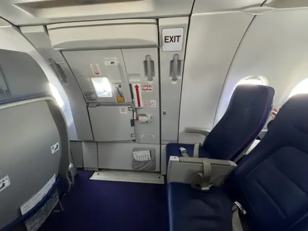 Wnętrze samolotu Wizzair. Widok na rząd siedzeń i drzwi wyjściowe. Numeracja miejsc w samolocie Wizzair jest widoczna na siedzeniach.