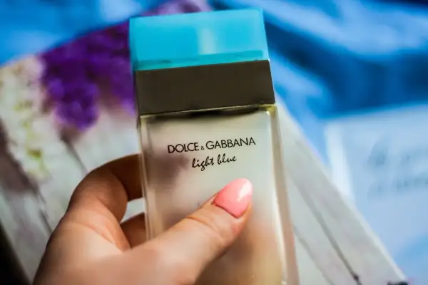 Dłoń z różowym lakierem trzyma buteleczkę perfum Dolce & Gabbana Light Blue.