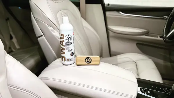 Zestaw do pielęgnacji jasnej skóry w samochodzie: butelka preparatu SWAG Leather Cleaner i drewniana szczotka. Idealne, by natłuścić skórę w samochodzie.