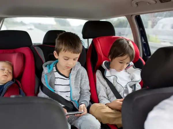 Im Auto mit 3 Kindern: Ein Baby schläft, die älteren Brüder sind mit ihren Handys beschäftigt.