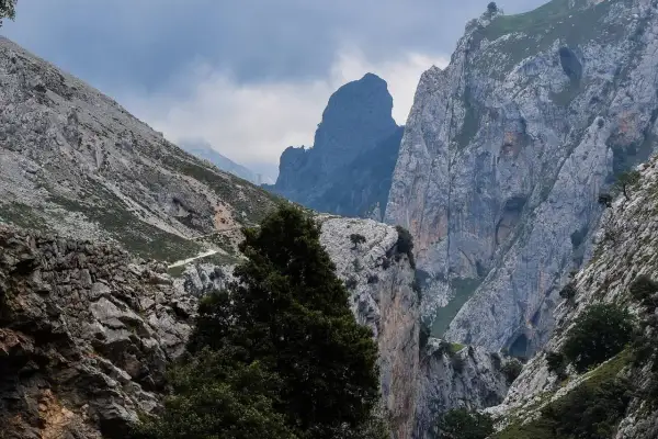 Majestuosas montañas y un camino serpenteante en la ruta del Cares, bajo un cielo nublado que presagia lluvia.
