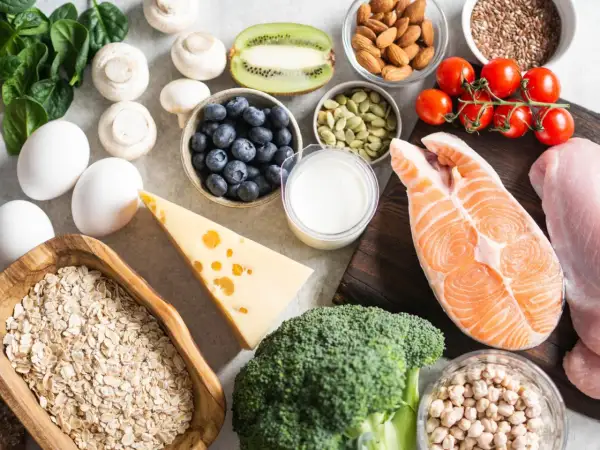 Vielfältige Lebensmittel für Muskelaufbau: Lachs, Hähnchen, Eier, Haferflocken, Beeren, Nüsse, Brokkoli, Käse und mehr.