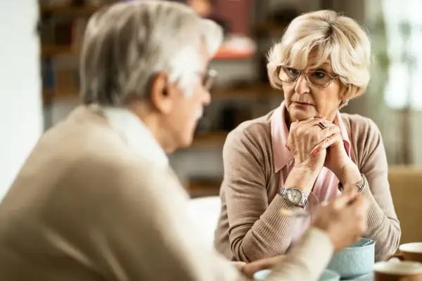 Un couple âgé discute, visiblement en désaccord familial au sujet d'une maison de retraite. La femme semble préoccupée.