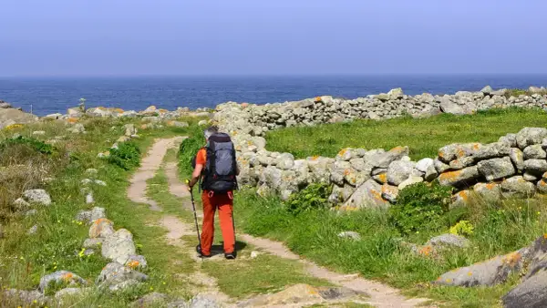 Pielgrzym z plecakiem idzie ścieżką wzdłuż kamiennego murku. Piękna trasa Santiago de Compostela nad oceanem.