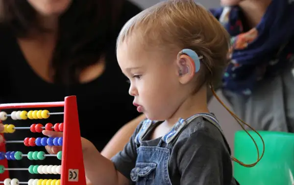 Niño con audífono jugando con ábaco, explorando la caja de los sentidos oido.