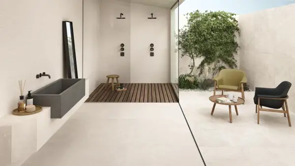 Bagno moderno con vasca in pietra, doccia a filo pavimento e un'area relax esterna. Il tipo di pavimentazione in gres porcellanato chiaro unifica gli spazi.
