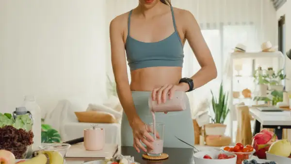 Frau mixt einen Smoothie, der zeigt, wie Proteinpulver beim Abnehmen helfen kann. Gesunde Zutaten liegen bereit.