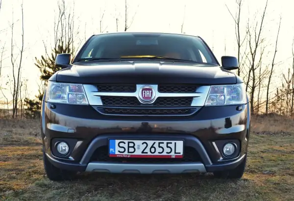 Czarny Fiat Freemont na tle drzew. Zastanawiasz się nad jego spalaniem? Ten SUV oferuje przestronne wnętrze i komfort podróżowania.