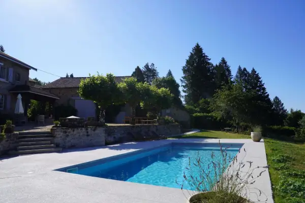 Belle propriété avec piscine, un projet de création bassin réussi. La maison en pierre et les arbres créent un cadre idyllique.