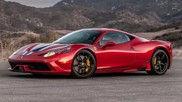 Czerwone Ferrari 458 z białymi i niebieskimi pasami na masce, zaparkowane na tle górskiego krajobrazu.