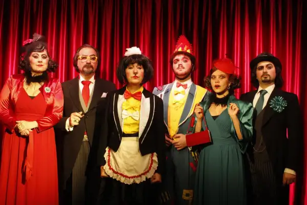 Sei personaggi in costume, forse per la cantatrice calva trama, posano davanti a una tenda rossa.