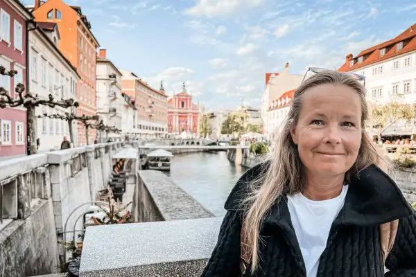 Kvinna ler vid floden i Ljubljana, Sloveniens huvudstad, med färgglada byggnader och en kyrka i bakgrunden.
