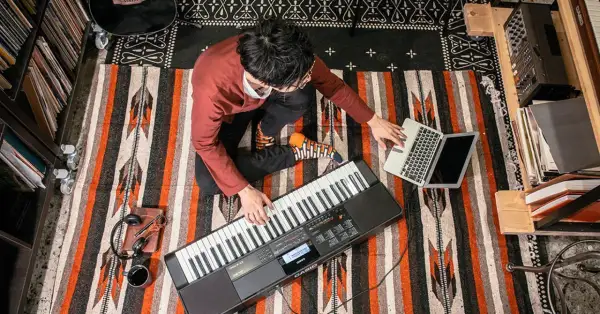 Mężczyzna gra na keyboardzie Casio, obok laptop i słuchawki.