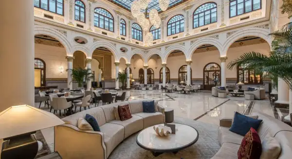 Elegante lobby del spa hotel Miramar, con sofás curvos, mesas y grandes lámparas de araña bajo un techo de cristal.