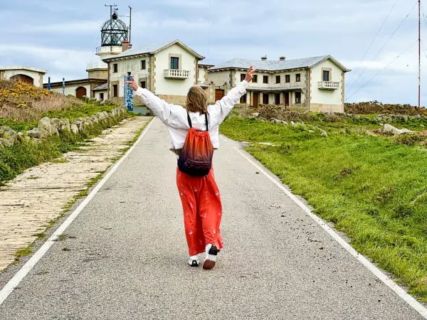 Persona con los brazos en alto camina por un camino hacia un faro y edificios. Parece una estaca de bares, pero es un lugar histórico.