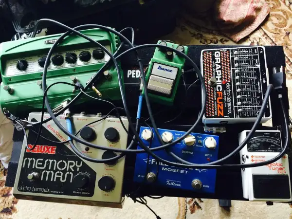 Pedalboard z efektami gitarowymi: zielony delay, srebrny Memory Man, niebieski Fulltone, czarny Electro-Harmonix i biały tuner.