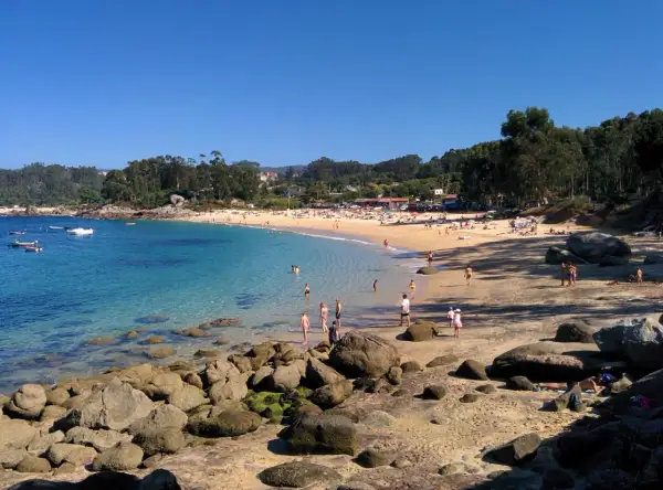 Gente disfrutando del sol y el mar en la Praia da Mourisca, con aguas cristalinas y arena dorada.