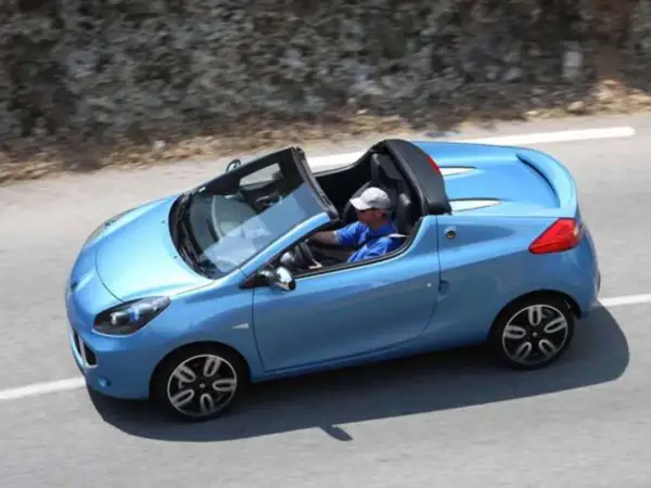 Niebieski kabriolet Renault Wind z otwartym dachem, kierowca w czapce i niebieskiej koszulce jedzie po krętej drodze.