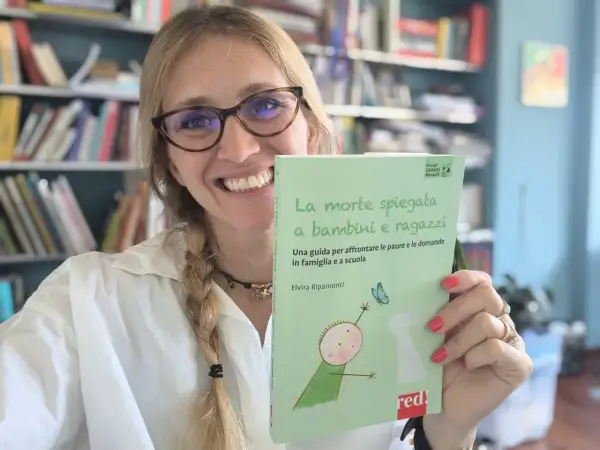 Donna sorridente con libro "La morte spiegata a bambini e ragazzi", affronta la paura di morire e lasciare i figli.