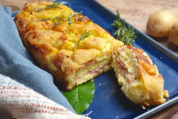 Polpettone di patate dorato e invitante, con strati di prosciutto e formaggio, guarnito con rosmarino e timo.