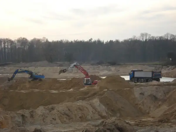 Koparki i wywrotka pracują na placu budowy, wykonując prace ziemne.