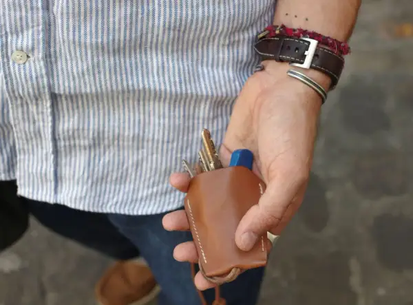 Main d'un homme au style workwear, tenant un étui à clés en cuir marron.