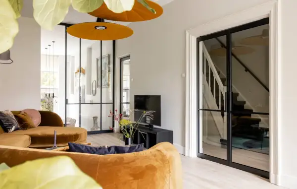 Gezellige woonkamer met oranje bank, glazen deuren naar de trap en een ontspullen lijst.