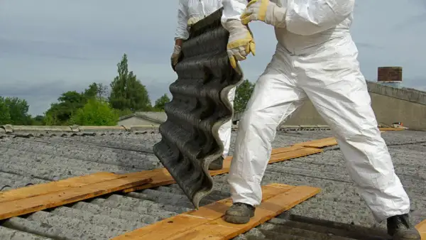 Arbeiter in Schutzanzügen entfernen eine Wellplatte. Bis in die 1990er Jahre wurde Asbest verbaut.