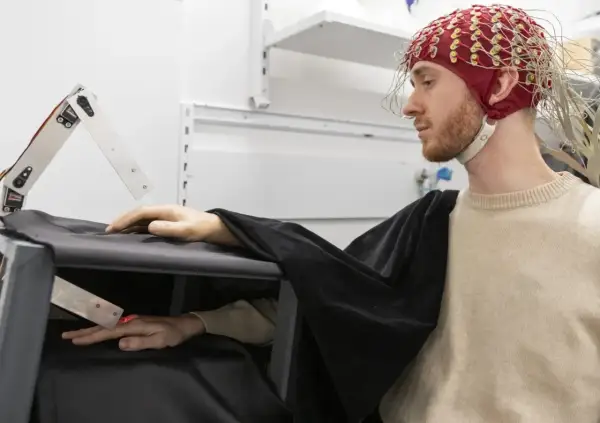 Joel Svenningsson med EEG-hjälm och en robotarm som interagerar med hans hand.