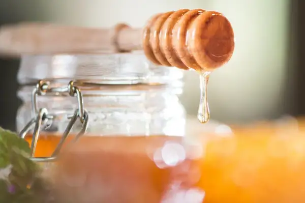 Ein Holzlöffel tropft goldenen Akazienhonig in ein Glas. Dieser Honig ist nicht nur süß, sondern auch gesund.