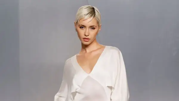 Iris Law, con su corte de pelo rubio platino y un elegante vestido blanco, posa con una mirada cautivadora.