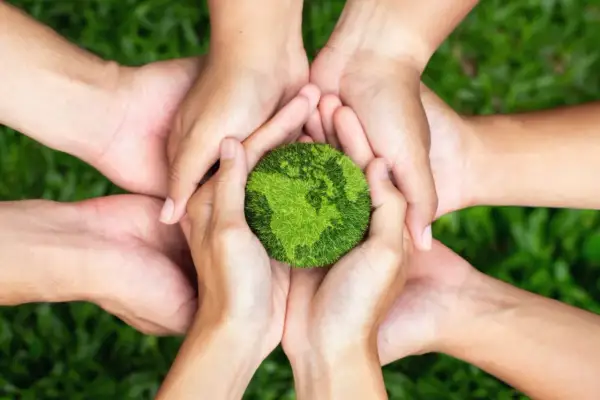 Viele Hände halten eine grüne Erde, die für Nachhaltigkeit steht. Gemeinsam können wir die Welt schützen und master sustainability.