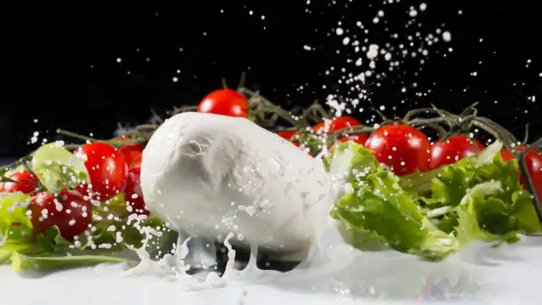 La mozzarella fresca, circondata da pomodorini e lattuga, viene spruzzata con latte in un movimento dinamico.