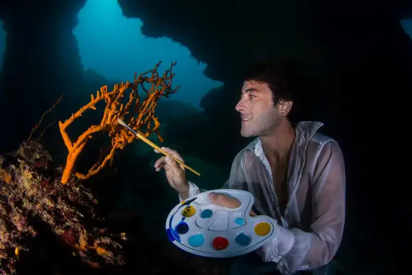 Un artista subacqueo crea foto creative, dipingendo un corallo arancione con una tavolozza colorata.