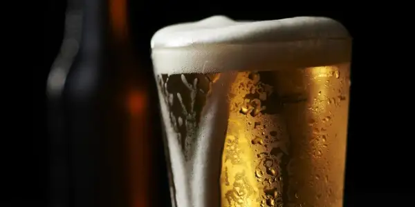 Bicchiere di birra olandese dorata con schiuma bianca e goccioline di condensa, su sfondo scuro.