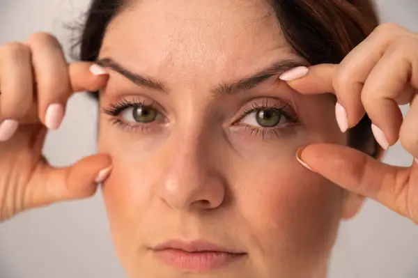 Une femme examine son visage, ses doigts effleurant sa peau. Elle semble préoccupée car j'ai des cernes noires sous les yeux.