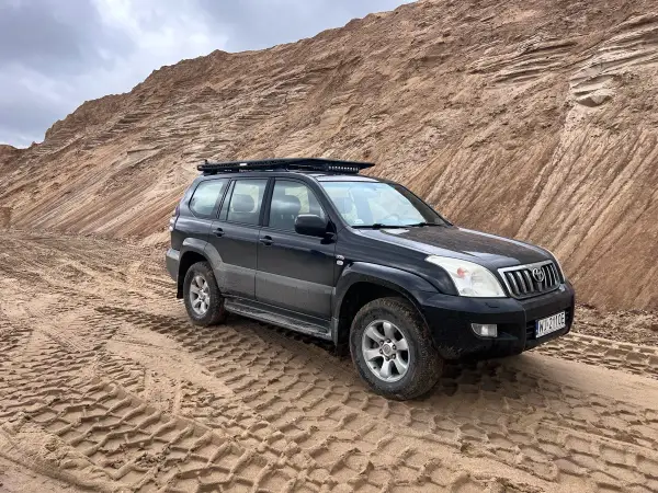 Czarny Land Cruiser 120 na piaszczystym podłożu, z bagażnikiem dachowym, gotowy na terenową przygodę.