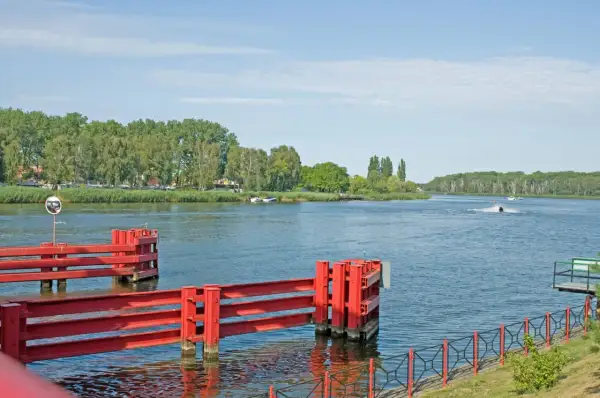 Czerwone śluzy wodne w Dziwnowie nad morzem, z zielonymi drzewami w tle i skuterem wodnym na wodzie.