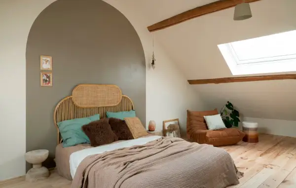 Gezellige slaapkamer verbouwen met rieten hoofdbord, zachte plaids en een comfortabele fauteuil onder het dakraam.