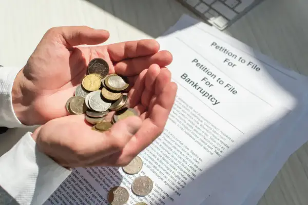 Dłonie trzymają garść monet obok dokumentu "Petition to File For Bankruptcy". To obrazuje, co się dzieje po ogłoszeniu upadłości konsumenckiej.