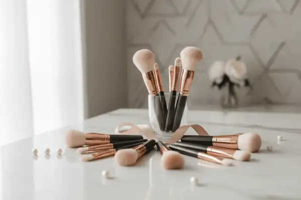 Un ensemble de pinceaux de maquillage aux manches noirs et dorés, disposés en cercle sur une table marbrée. Un ruban rose pâle les entoure, rappelant l'importance de nettoyer pinceau maquillage pour une peau saine.