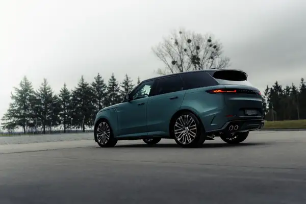 Elegancki, zielony Range Rover, jeden z prestiżowych angielskich marek samochodów, parkuje na tle drzew.