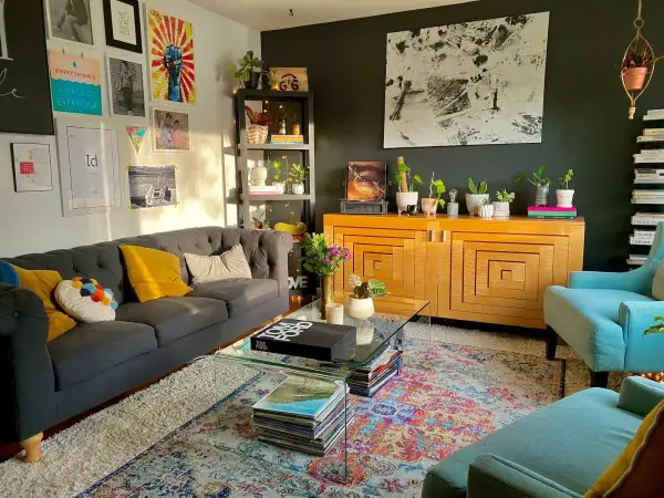 Salon w stylu maksymalistycznym: szara sofa, turkusowe fotele, kolorowy dywan, mnóstwo roślin i dekoracji na ścianach.