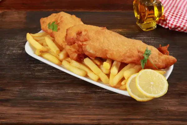 Un delicioso plato típico inglés: pescado rebozado y patatas fritas crujientes, servido con rodajas de limón y perejil.