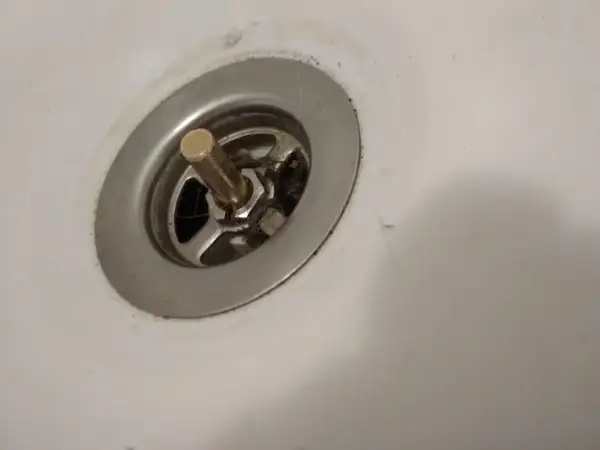 Korek do wanny z pokrętłem, widoczny mechanizm do naprawy. Widać włosy i brud wokół odpływu.