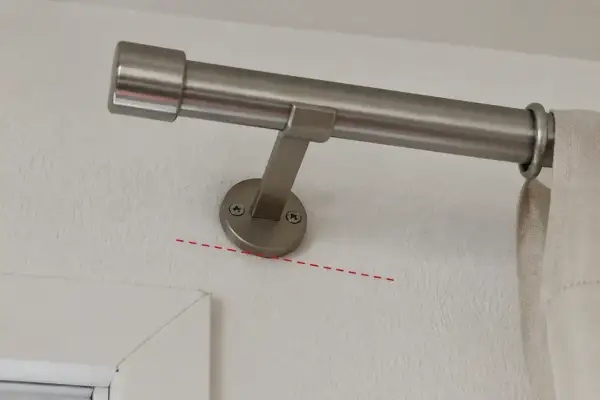 Eine silberne Gardinenstange wird an der Wand befestigt. Die Halterung ist mit Schrauben gesichert.